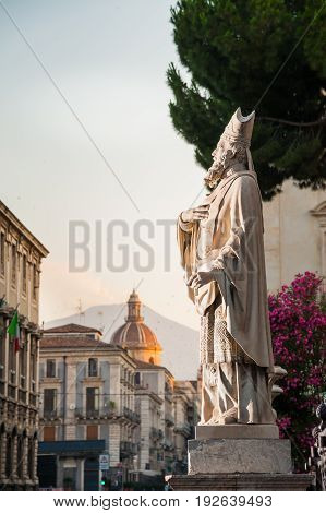 Statue outside the Church of St. Agatha in Catania Sicily with the town and Mount Etna in the background