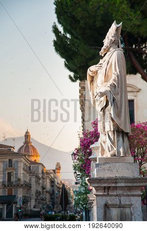 Statue outside the Church of St. Agatha in Catania Sicily with the town and Mount Etna in the background
