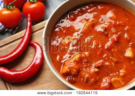Bowl with delicious chili turkey on wooden board, closeup