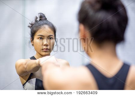 young asian athletic women in sportswear punching and looking herself in the mirror