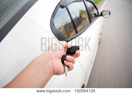 Hand of man holding and push remote control car alarm systems at car park .