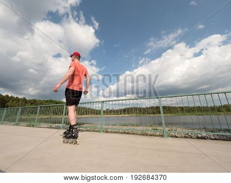 Roller Skater In Action. Man Ride In Inline Skates Ride Along Promenade Handrail, Sky In Background