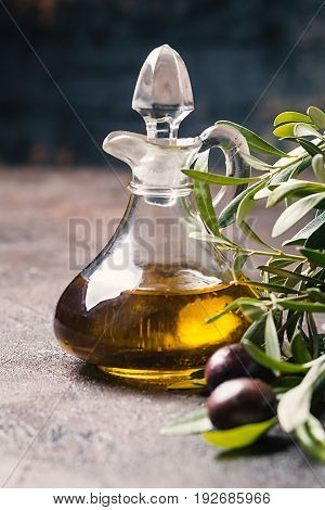 Olive oil in a glass bottle and olive branch on brown stone table
