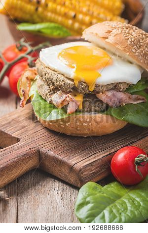 Homemmade Bacon Hamburger with fried Egg, Lettuce and lentil burger with a garnish of corn and tomatoes