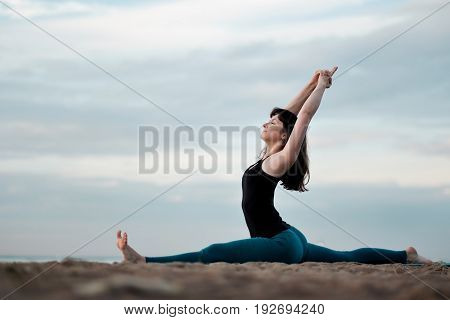 Caucasian young woman practicing yoga in nature hanumanasana monkey pose.