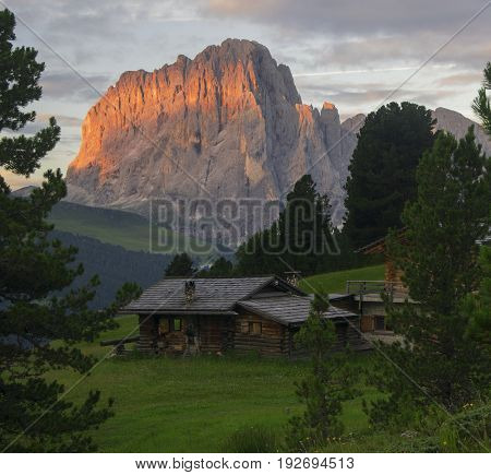 Mountain wooden house on Gardena Valley and sunlit mountains on background above Ortisei and St. Christina villages Dolomites Italy