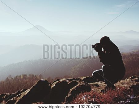Photographer  Look Down Into Fogy Valley. Man Is Kneeling On Cliff And Takes Photos.