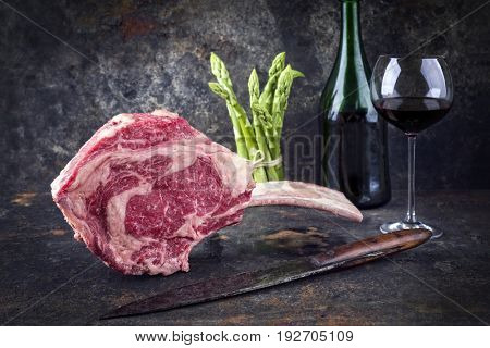 Raw dry aged Wagyu Tomahawk Steak with green asparagus and redwine as close-up on old metal sheet