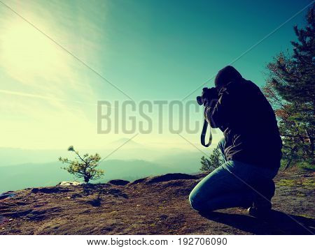Photographer  Look Down Into Fogy Valley. Man Is Kneeling On Cliff And Takes Photos.