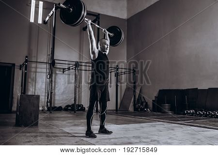 Black and white full length portrait of Strong man lifting a barbell during crossfit workout at gym.