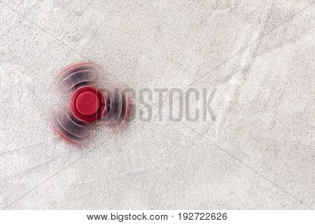 Red fidget spinner in motion stress relieving toy on concrete background.