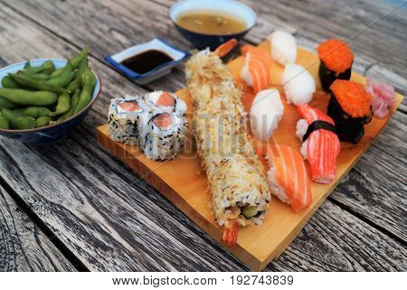 Sushi on wood table. Sushi meal scene featuring a light wood serving tray with nigiri sushi and sushi rolls, miso soup, edamame and soy sauce on a dark rustic wood table