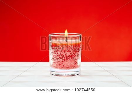 Aromatic red candle in a glass against red background