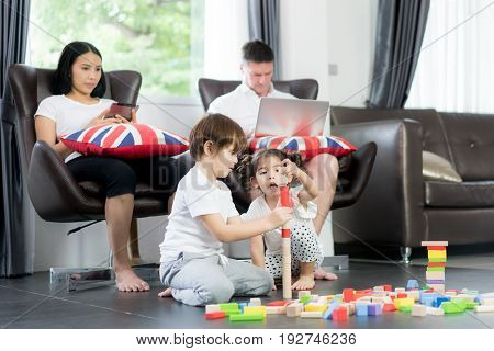 Asian brother and daughter playing wood toy in living room with father and mother in background. Happy family.