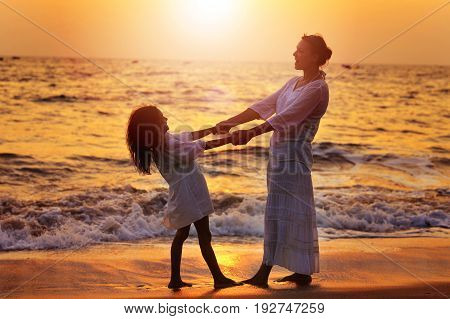 Mother and daughter on sandy beach during beautiful sunset