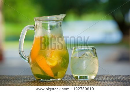 Jug of non-alcoholic drink and a glass of ice on a table with a blurred background.