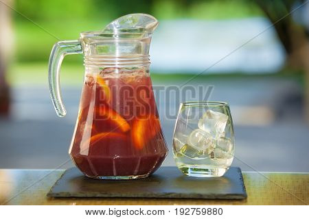 Jug of non-alcoholic drink and a glass of ice on a table with a blurred background.