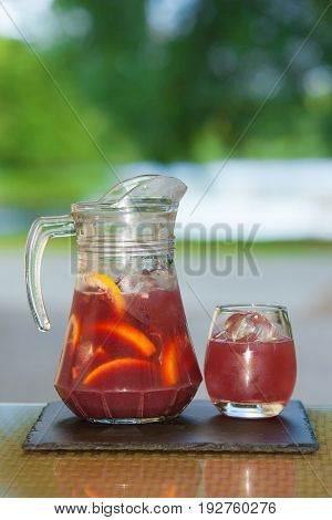 Jug of non-alcoholic drink and a glass of ice on a table with a blurred background.