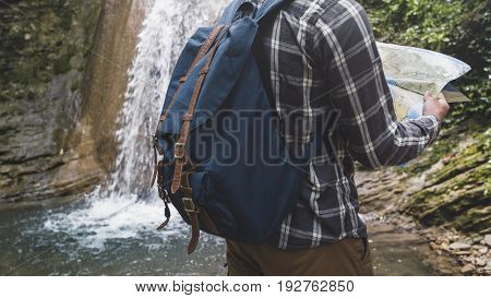 Traveler With A Backpack Is Standing By The Waterfall And Looks At The Map Holidays And Tourism Concept