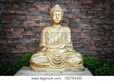 Golden Buddha statue against a brick wall background.