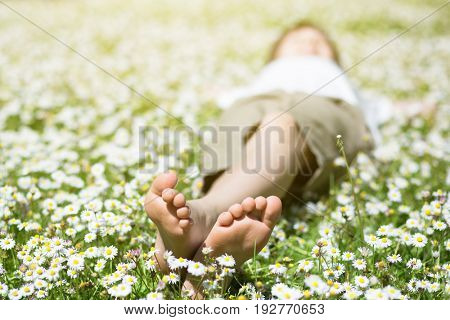 Child's feet in daisy closeup view. Shoeless boy. Little boy lying on summer meadow green grass with daisy. 