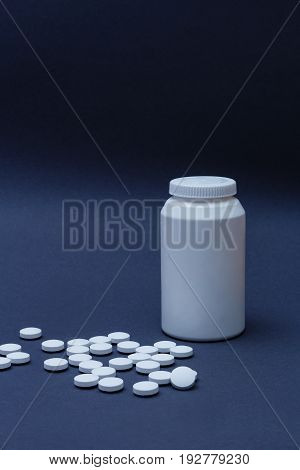 White pills medicine and plastic bottle behind on dark gradient background