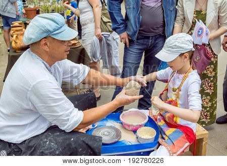 Zaporizhia/Ukraine- May 28, 2017: Charity Family festival:  Outdoors pottery workshop - ceramist master helps girl to cut a piece of clay with a string. Art and craft activity.