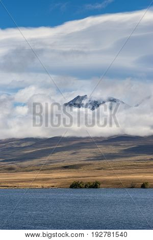 Middle Earth New Zealand - March 14 2017: Portrait with focus on Volcano Potts behind blue Lake Clearwater. All under blue cloudy sky.
