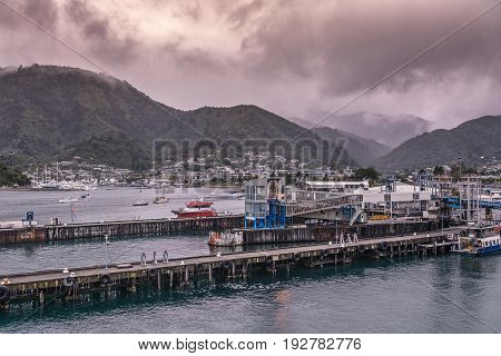 Picton New Zealand - March 12 2017: Picton commercial and ferry port with the town in the back on the of tall green mountains under heavy brown cloudscape.