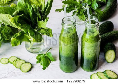 Detox diet. Two small bottles of fresh green smoothies with ingredients on a light wooden background