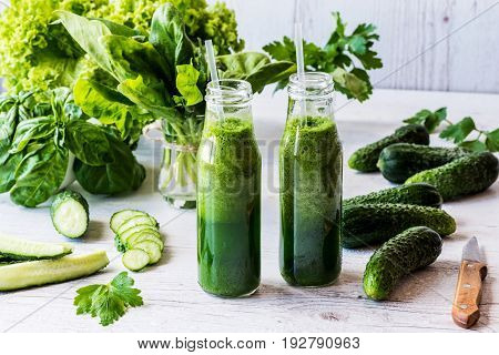 Detox diet. Two small bottles of fresh green smoothies with ingredients on a light wooden background