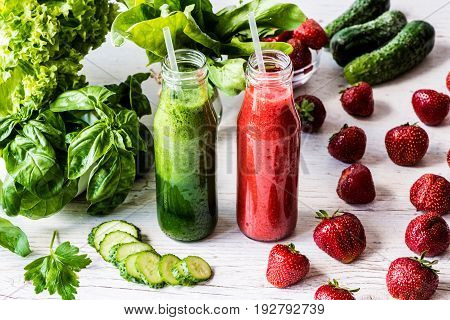 Green smoothie and strawberry smoothie in two small bottles with ingredients on a light wooden background. Healthy detox drinks