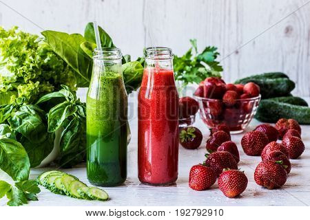 Green smoothie and strawberry smoothie in two small bottles with ingredients on a light wooden background. Healthy detox drinks