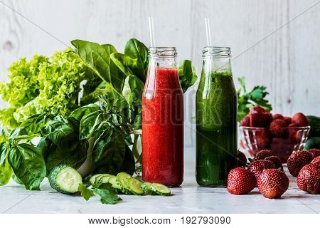 Green smoothie and strawberry smoothie in two small bottles with ingredients on a light wooden background. Healthy detox drinks