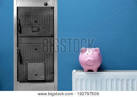 Energy savings concept. Solid fuel boiler and radiator with piggy bank on color background