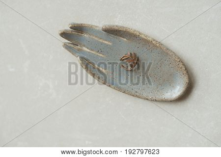 Top view on chamotte clay blue and grey rustic hand holding beautiful twig ring on grey industrial table