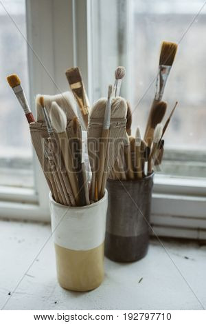 Pottery tools brushes with wooden holders in ceramic vases on windowsill in pottery studio
