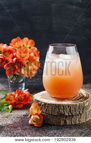 Floral pastel peach and pink brunch cocktail garnished with quince flowers over old rustic background.