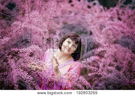 Portrait of a middle-aged woman in pink flowers of tamaricaceae. Beautiful romantic woman in Tamarix