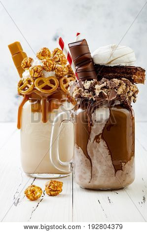 Caramel and chocolate indulgent extreme milkshakes with brezel waffles popcorn marshmallow ice cream and whipped cream. Crazy freakshake food trend.