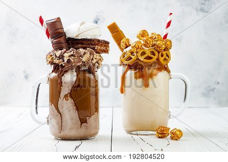 Caramel and chocolate indulgent exreme milkshakes with brezel waffles popcorn marshmallow ice cream and whipped cream. Crazy freakshake food trend.