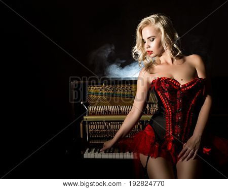Young beautiful girl in red corset standing near the piano. Vintage style beautiful woman. Old fashioned makeup and retro finger wave hairstyle.