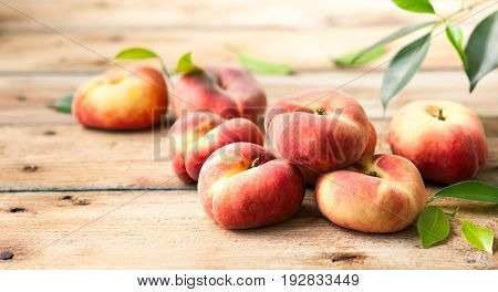 Fresh peaches with leaves on wooden background. Doughnut or vineyard type of flat peach.
