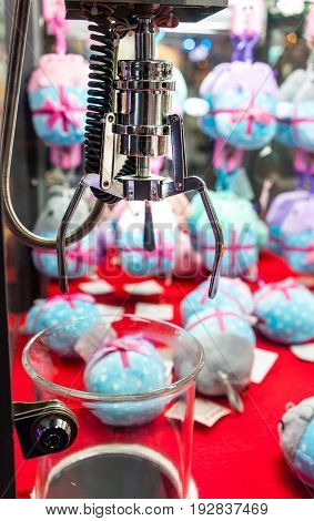 Mechanic claw crane for grabbing soft toy in doll vending machine at game center. Robotic arms with clamp over plastic dispenser for controller.