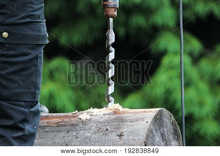 The worker collects the frame and drills a hole in a log for dowel using a drill when building a wooden house.