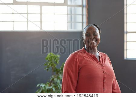 Portrait of a casually dressed young African businesswoman smiling confidently while standing alone in a bright modern office