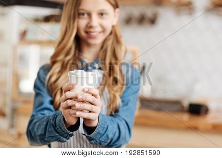 Delicacy of hands. The focus being on dainty neat hands of a charming young barista holding a while cup of hot coffee with her both hands while looking at the camera with pleasant smile