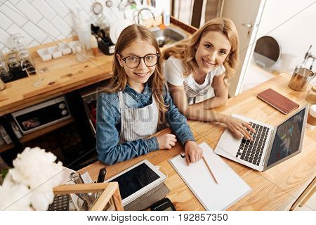 Family business. Charming fair-haired mother and daughter standing behind the coffee bar counter and working on the development program of their common business