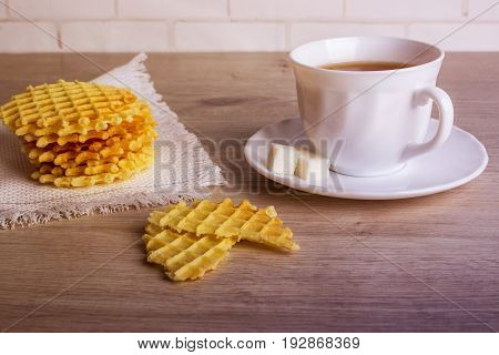 Breakfast With White Cup Of Black Tea With Waffles Stack On Napkin And Pieces Of Waffle On Wooden Su