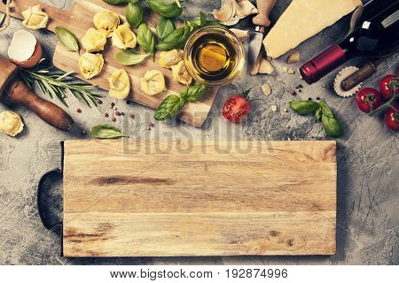 Italian food background with ravioli, vine tomatoes, basil, spaghetti, spinach, onion, parmesan, olive oil, garlic, peppercorns, rosemary and wine. Slate background 